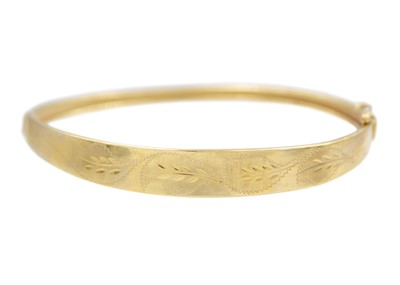 Lot 145 - A 9k oval hinged bangle with leaf-cut decoration.
