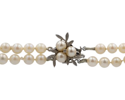 Lot 23 - A double-row cultured pearl necklace, strung to a 14k white gold diamond and pearl set clasp.