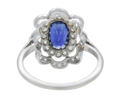 Lot 8 - An Art Deco oval blue sapphire and millgrain diamond set white metal cluster ring.