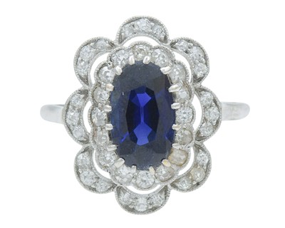 Lot 8 - An Art Deco oval blue sapphire and millgrain diamond set white metal cluster ring.