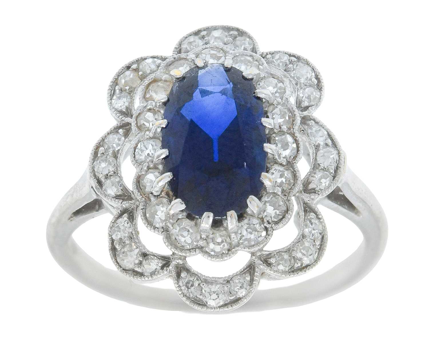 Lot 8 - An Art Deco oval blue sapphire and millgrain diamond set white metal cluster ring.