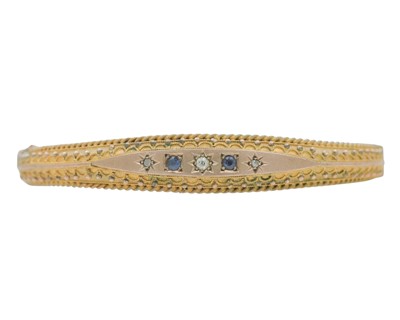 Lot 3 - An Edwardian 9k rose gold Etruscan Revival diamond and blue gem set hinged bangle.