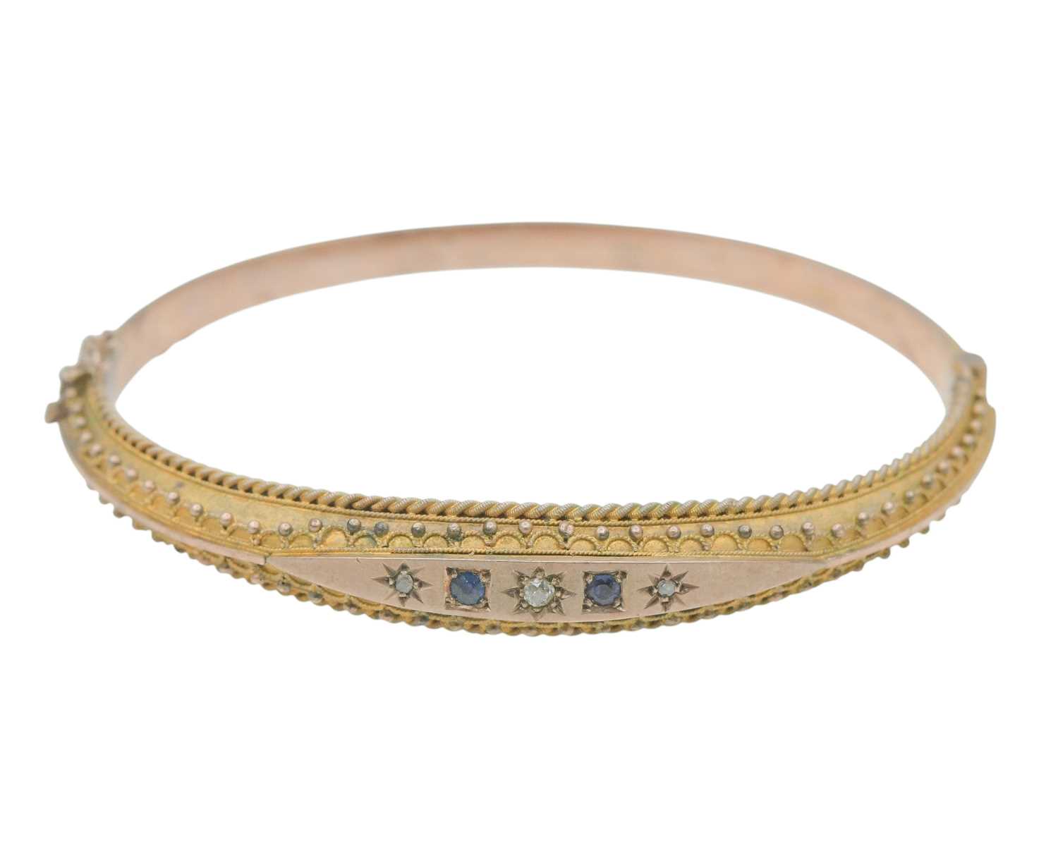 Lot 3 - An Edwardian 9k rose gold Etruscan Revival diamond and blue gem set hinged bangle.