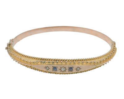 Lot 3 - An Edwardian 9k rose gold Etruscan Revival diamond and blue gem set hinged bangle.