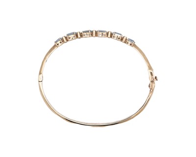 Lot 16 - An attractive 9k hallmarked gold oval cut aquamarine and diamond set hinged bangle.