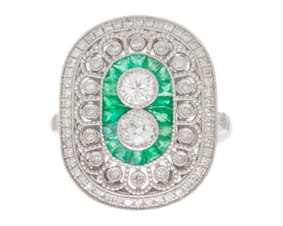 Lot 105 - An ornate platinum oval panel ring with diamonds and calibre cut emeralds.