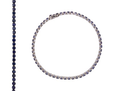Lot 139 - A 18k white gold line bracelet set with round dark blue sapphires.