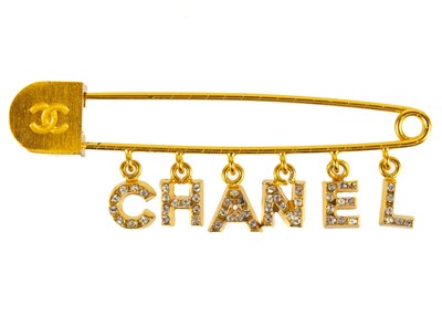 Lot 354 - A Chanel gold tone pin brooch with crystal set charm logo.